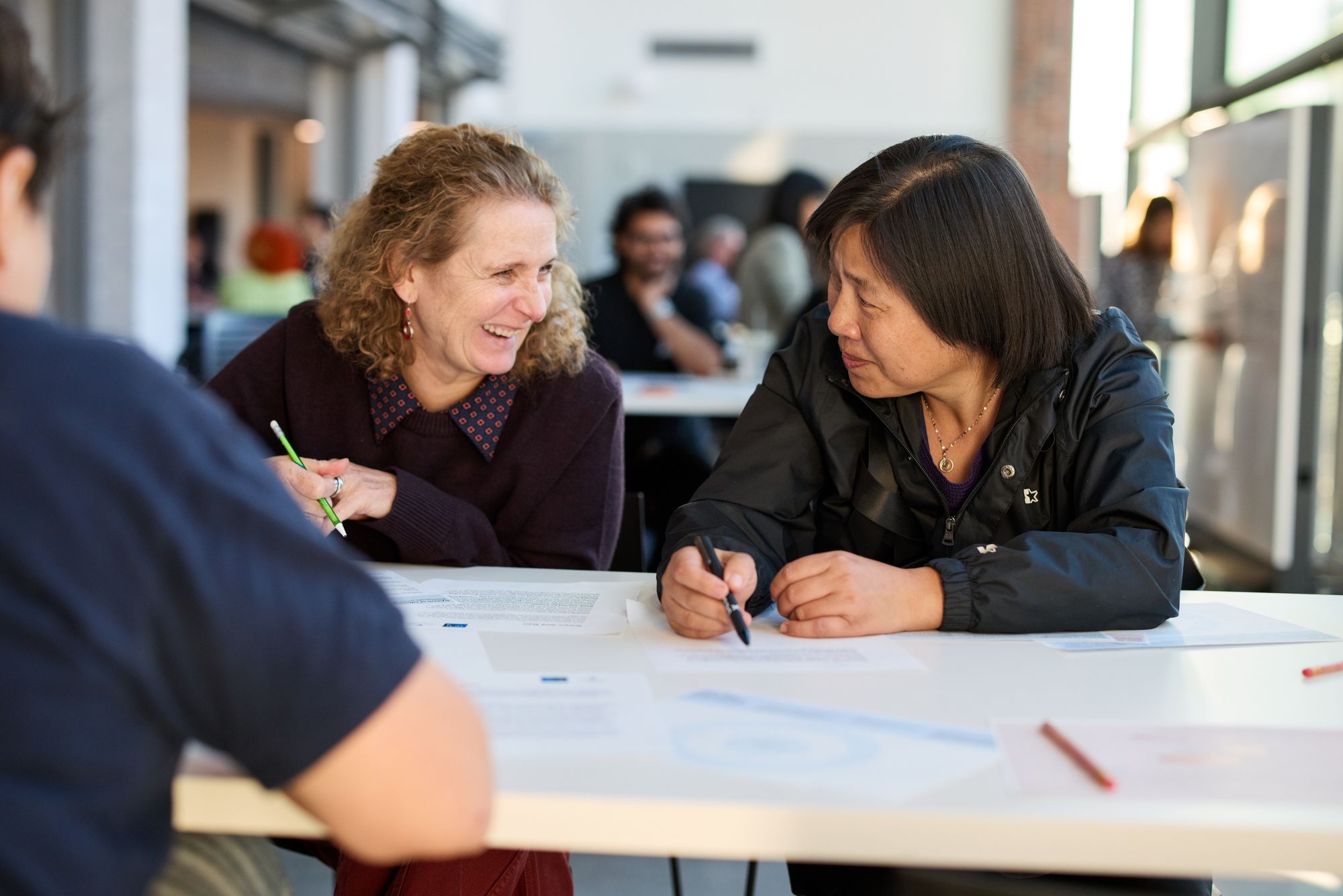 Two participants laugh together as they lean over their worksheets.